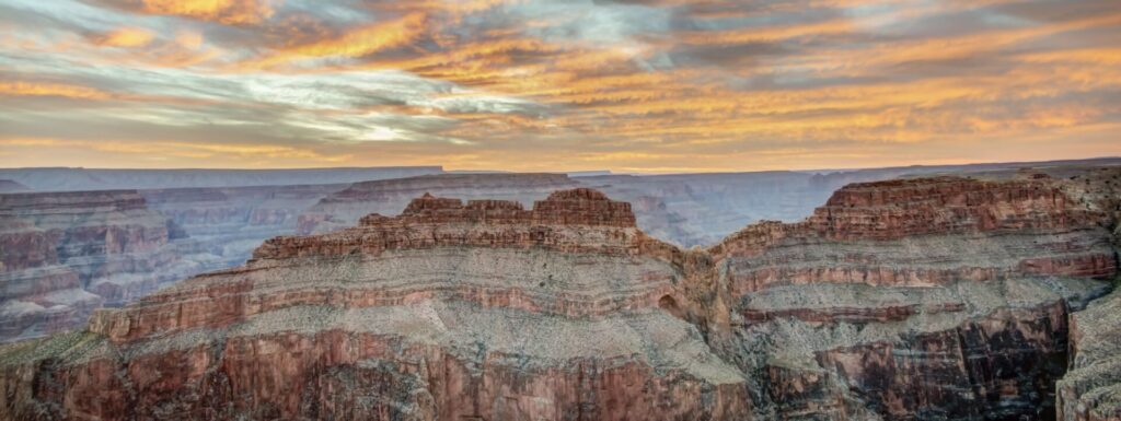 Pointe de l'Aigle A dramatic sunset or sunrise sky with orange and yellow clouds hangs over the vast, layered Grand Canyon.