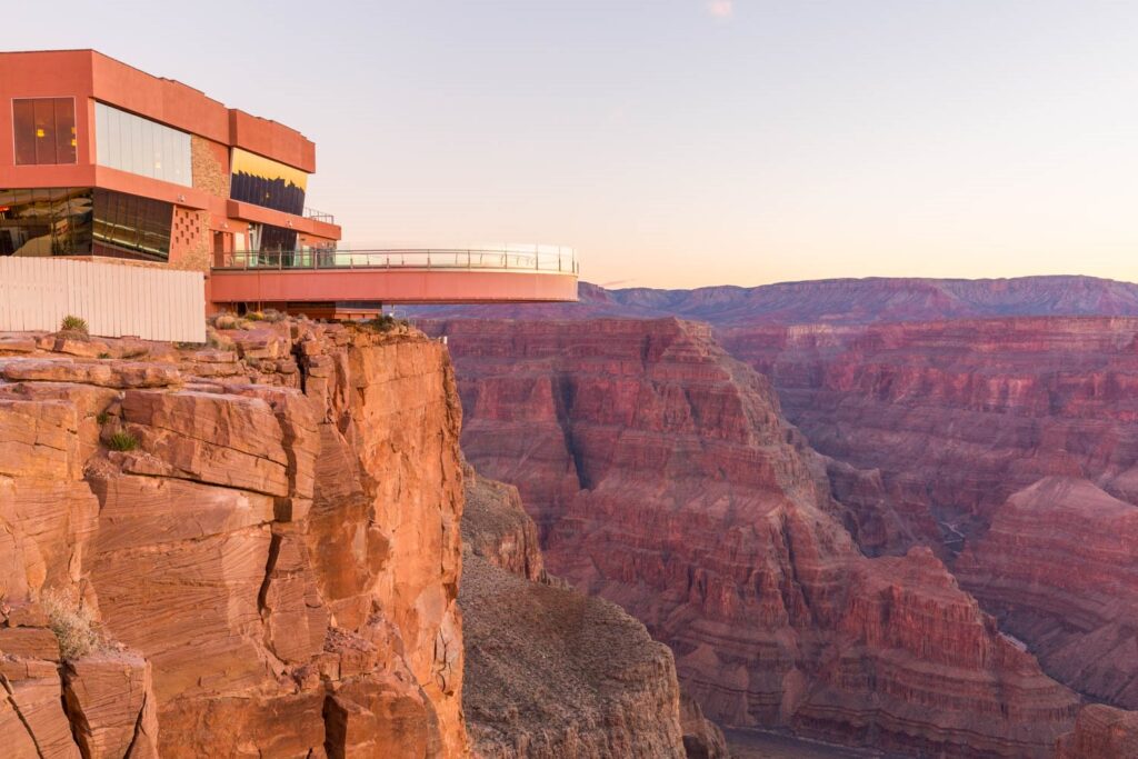 Passerelle aérienne A glass skywalk extends from a modern building over the Grand Canyon at sunset or sunrise.