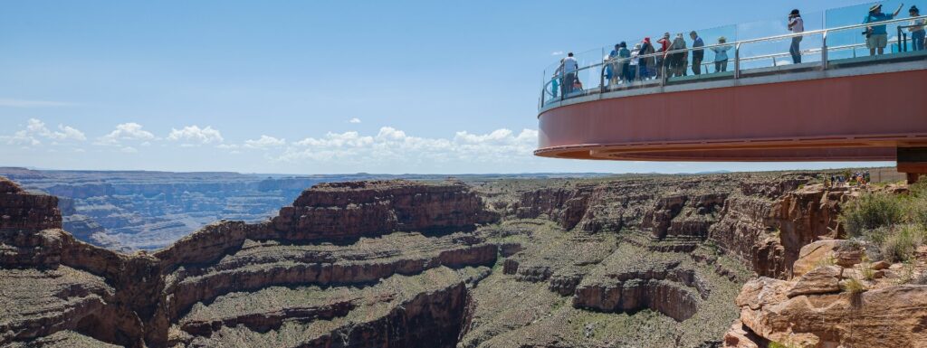 Passerelle aérienne A panoramic view of the Grand Canyon shows the Skywalk on the right, with people looking out over the vast landscape.