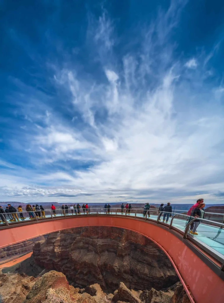 People on the horseshoe-shaped Grand Canyon Skywalk under a dramatic cloudy sky.